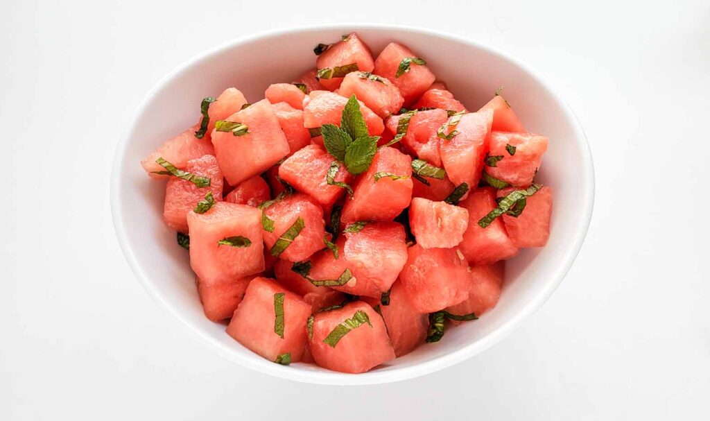 Flat lay shot of a bowl of cubed watermelon with chopped mint leaves.