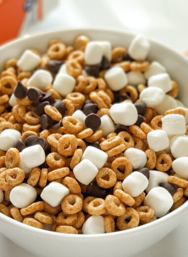 white bowl of cheerio, marshmallows and chocolate chips with cheerios box and halloween theme goody bags in the background
