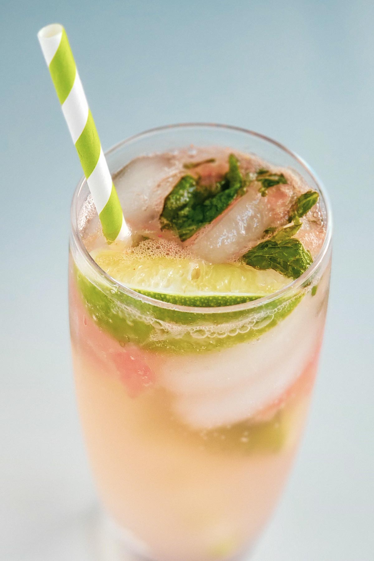 glass filled with mojito and ice, lime wedges, mint, and a green and white striped straw