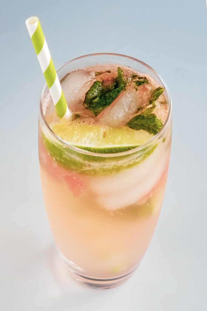 cocktail glass with watermelon mojito, ice, lime, mint, and a green and white striped straw