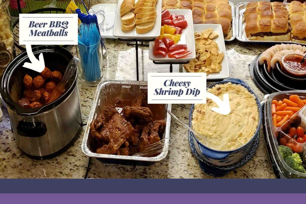 Variety of foods on counter highlighting the BBQ Beer Meatballs in a slow cooker and the Cheesy Shrimp Dip in a blue oval casserole dish