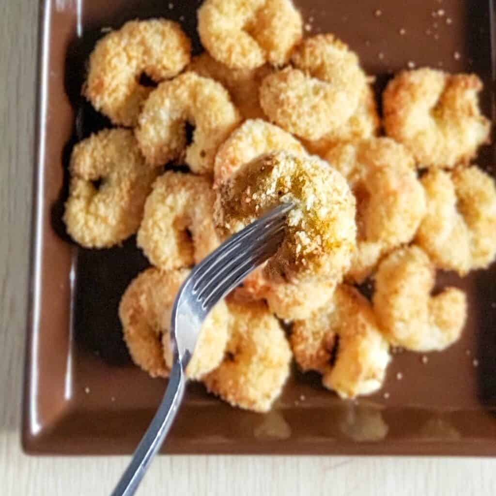 crispy breaded shrimp piled onto a square brown plate with a silver metal fork holding up one shrimp