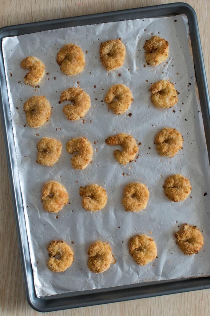 Breaded baked shrimp lined up on a layer of tinfoil on a baking sheet