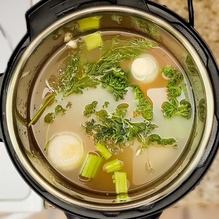 Top down view into Instant Pot showing water with herbs and veggies ready to cook.