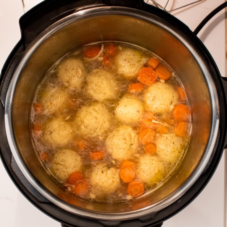 Top down view into Instant Pot with matzo balls boiling in broth with carrots.