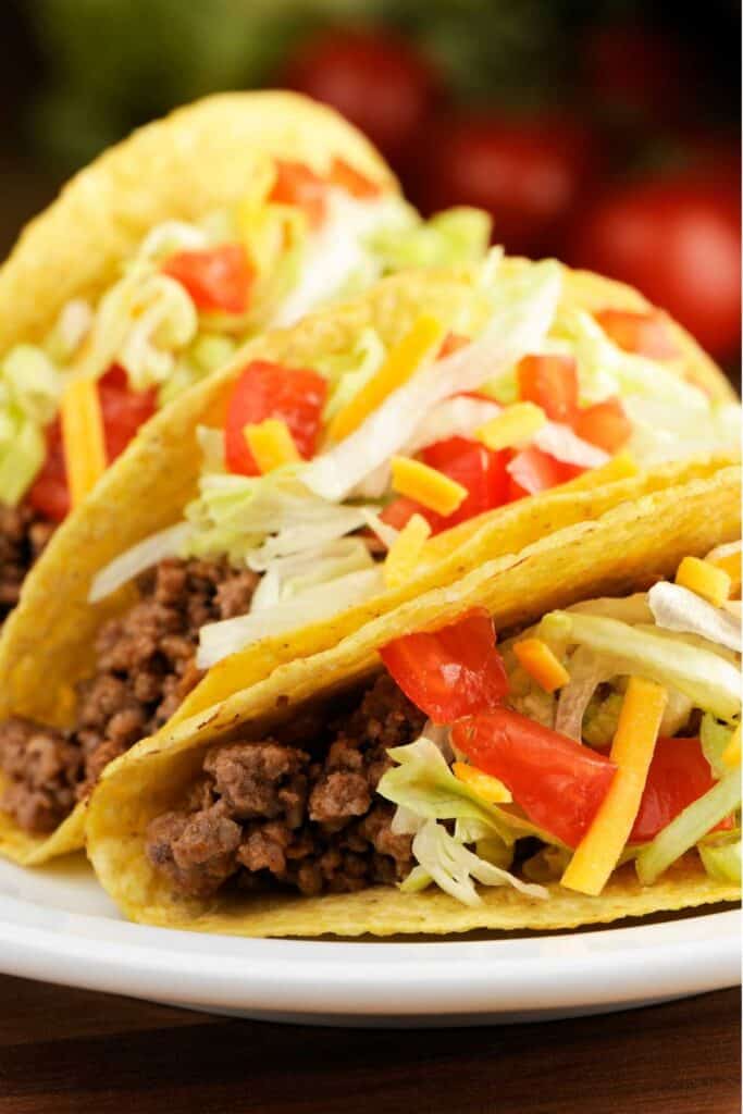 close up of three ground meat tacos with lettuce tomato and cheese