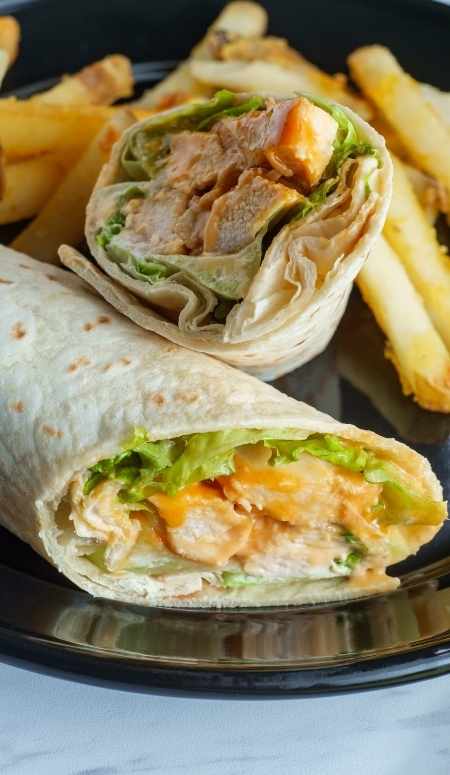 plate with a buffalow chicken wrap cut in half and stacked and some french fries