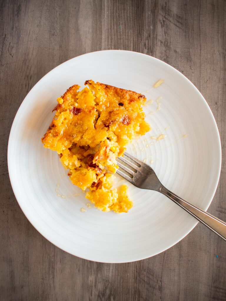 white plate with a square slice of corn casserole and a fork digging into it