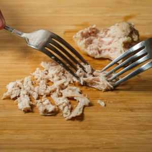 two forks shredding chicken on a wooden cutting board