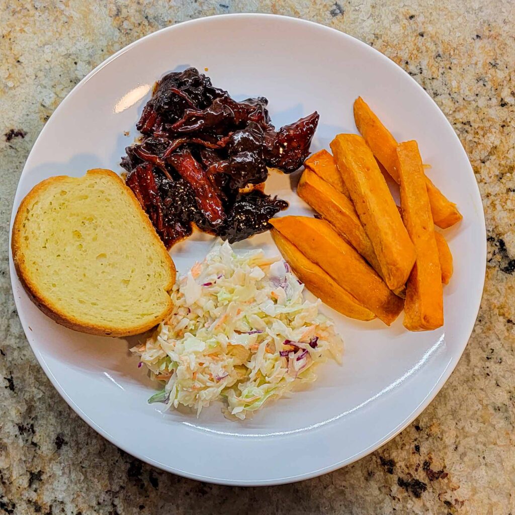 white plate with texas toast, sweet potato wedges, cole slaw, and bbq beef
