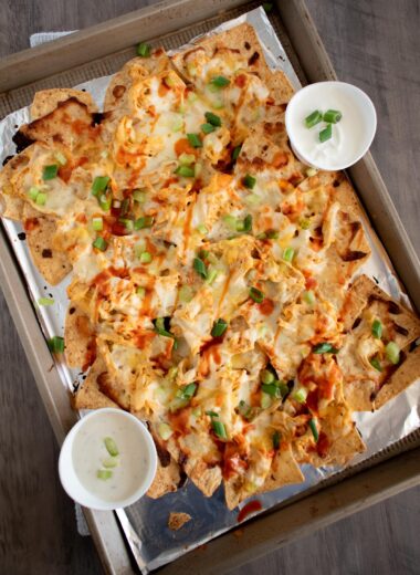 sheet pan of buffalo chicken nachos with two small dishes of sour cream and ranch.