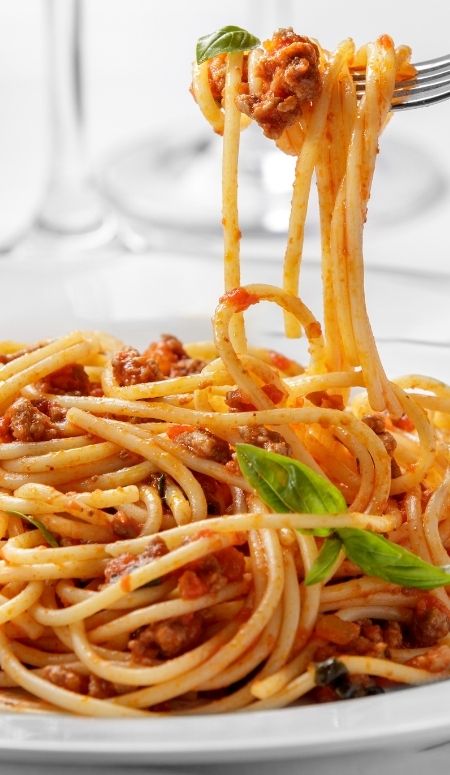 white plate of spaghetti with fork lifting up a bite of spaghetti.