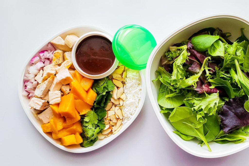 bowl with spring mix and plate with remaining salad ingredients as well as a container with dressing.