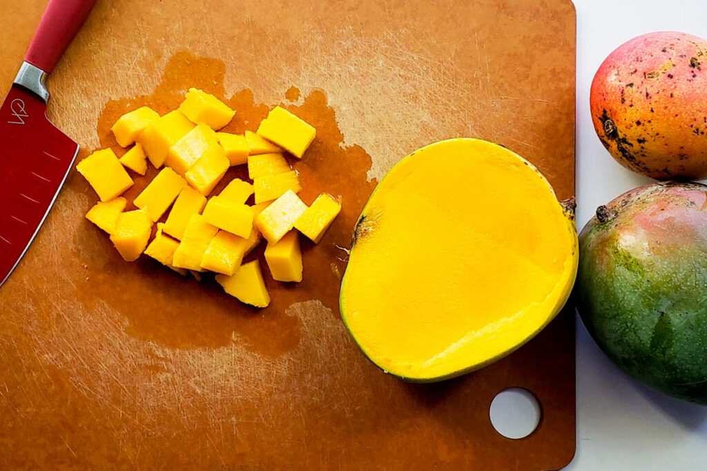 cutting board with diced mango and a half mango.