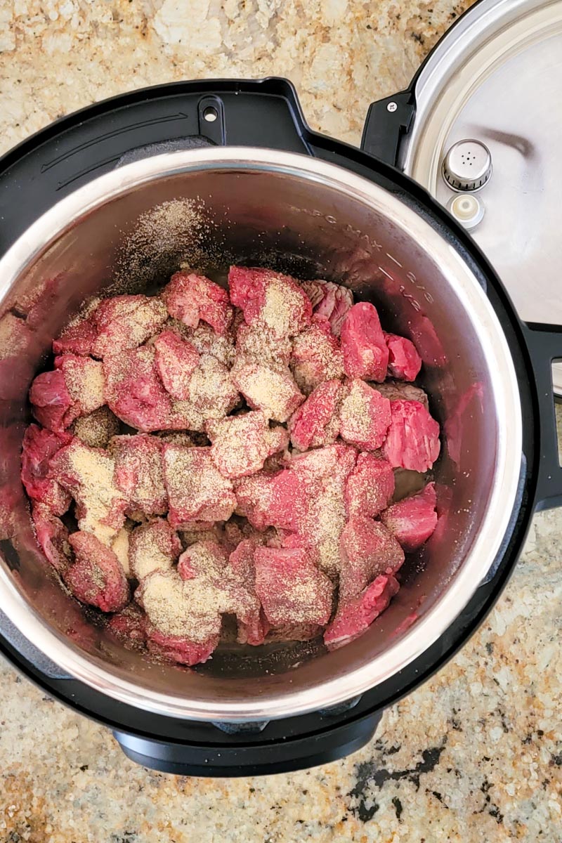 inside of instant pot with cubes of raw beef sprinkles with seasonings.