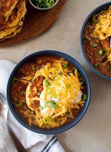 bowls of chili topped with a corn cake sour cream green onions and scallions.