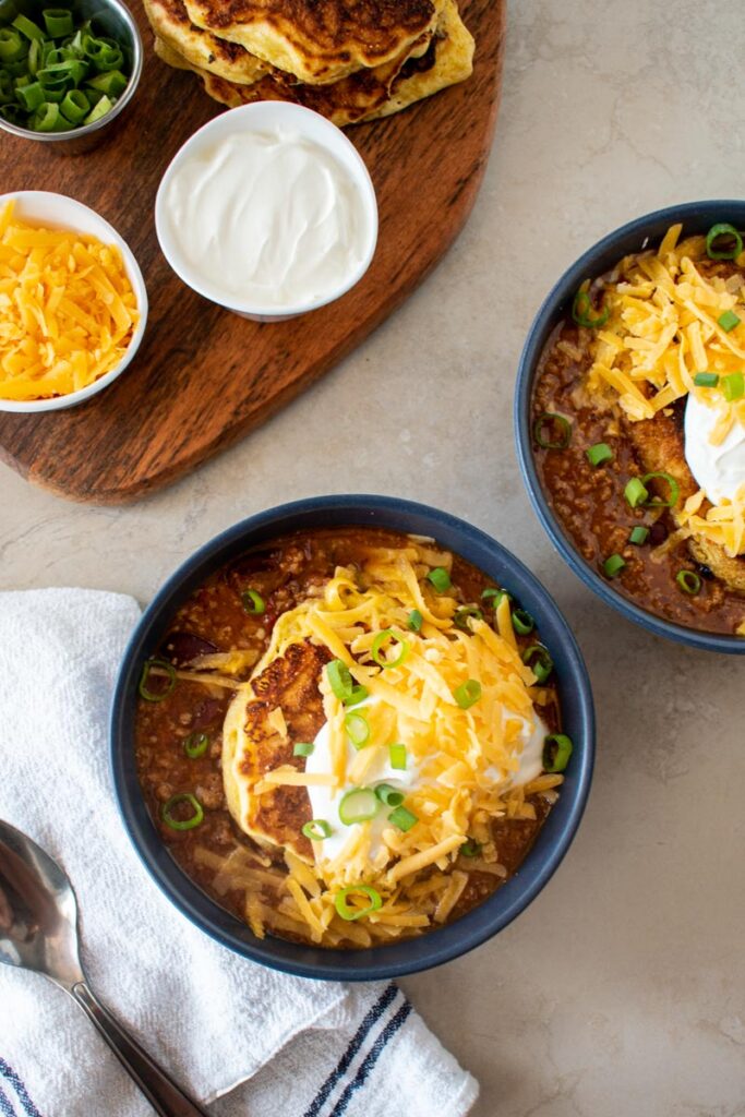 two bowls of chili and a board with small bowls of various toppings.