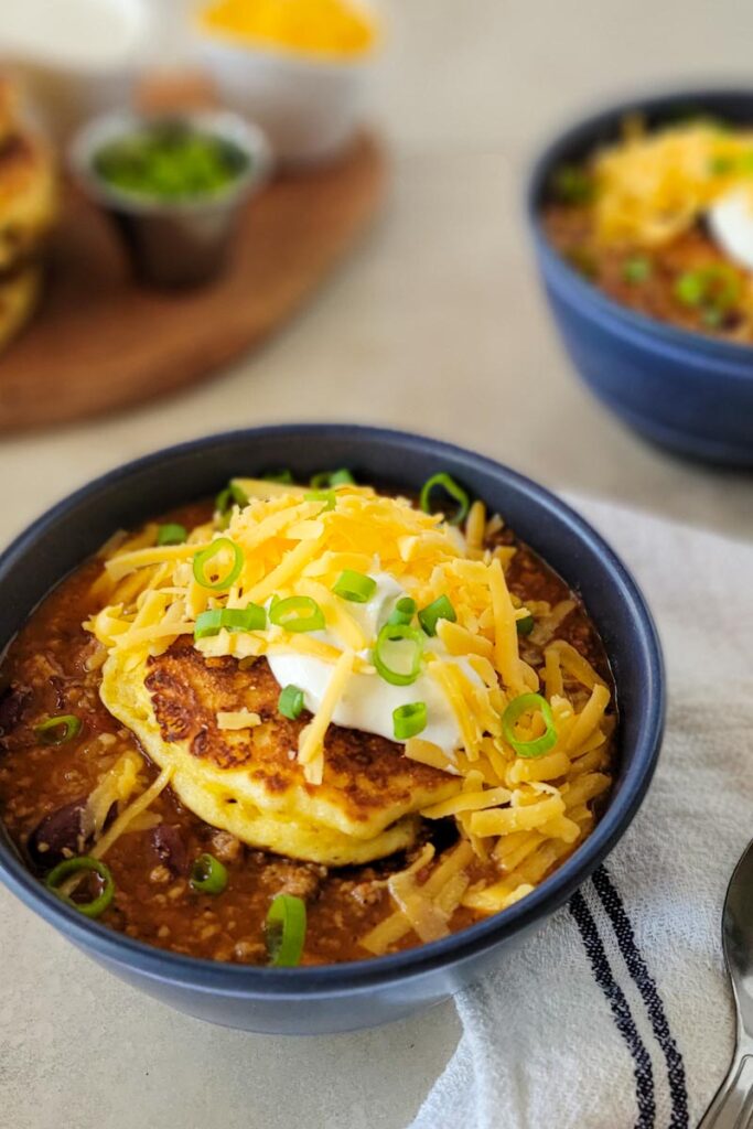 bowls of chili topped with a corn cake sour cream green onions and scallions.