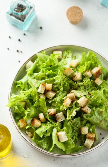 bowl of green leaf lettuce with croutons, bottle of olive oil and pepper shaker on the side.