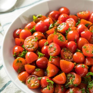 white bowl of halved grape tomatoes tossed with parsley.