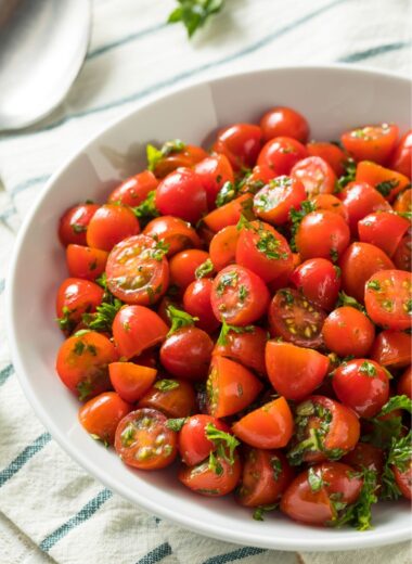 white bowl of halved grape tomatoes tossed with parsley.