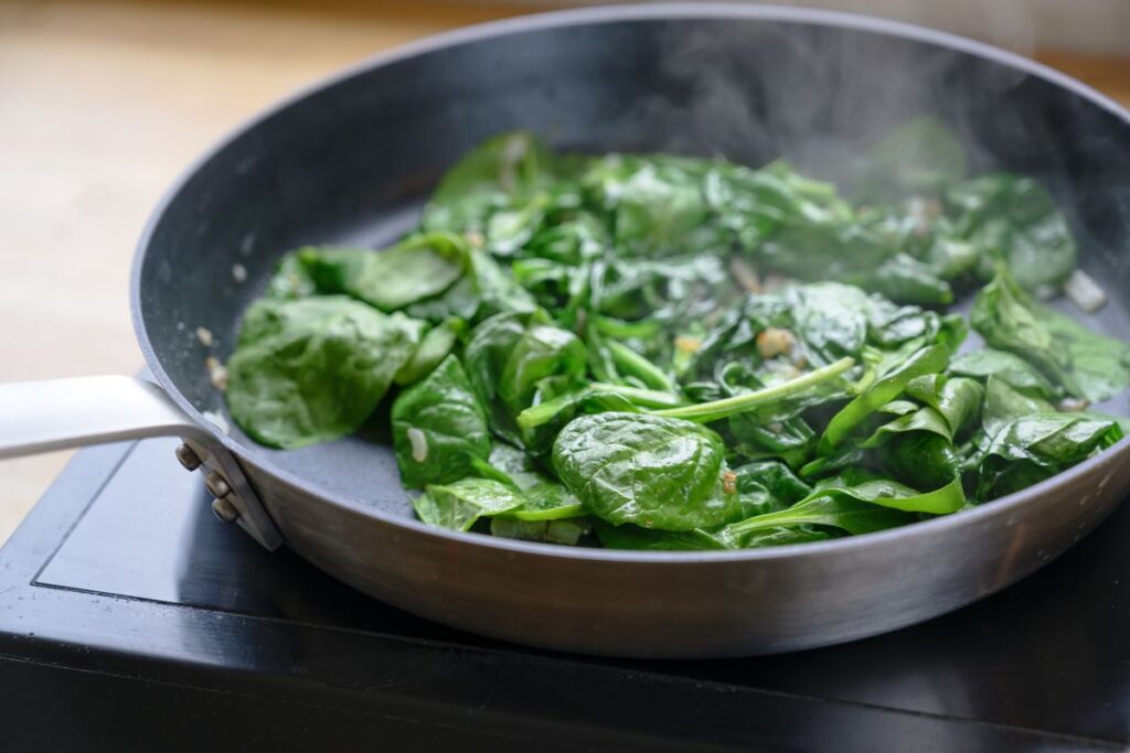 nonstick skillet with semi-wilted spinach, steam rising from pan.
